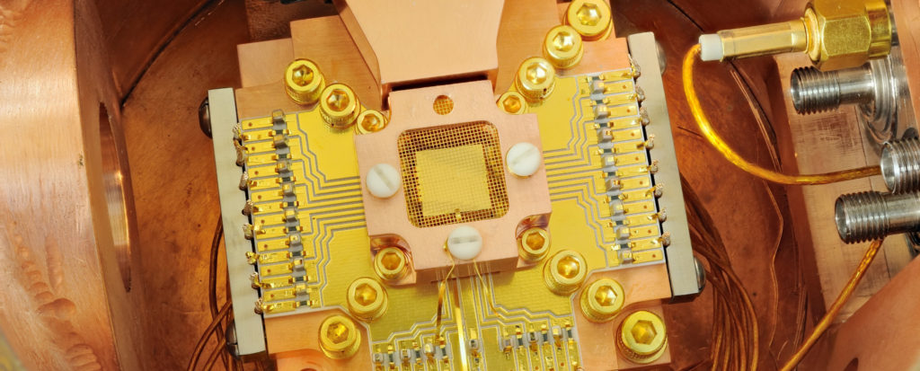 Two beryllium ions trapped 40 micrometers apart from the square gold chip in the center form the heart of this ‘trapped ion’ quantum computer. (Photo: Y. Colombe/NIST)